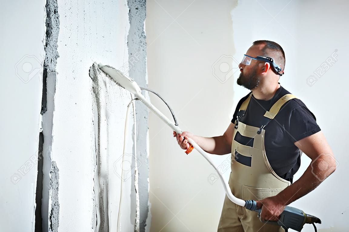 Plasterer using screeder spraying putty plaster mortar on wall