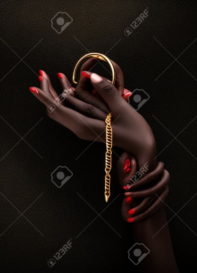Black woman's hand with gold jewelry. Oriental Bracelets on a black painted hand. Gold Jewelry and luxury accessories on black background closeup. High Fashion art concept