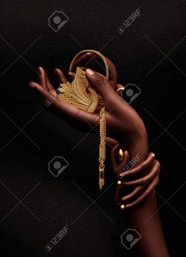 Black woman's hand with gold jewelry. Oriental Bracelets on a black painted hand. Gold Jewelry and luxury accessories on black background closeup. High Fashion art concept