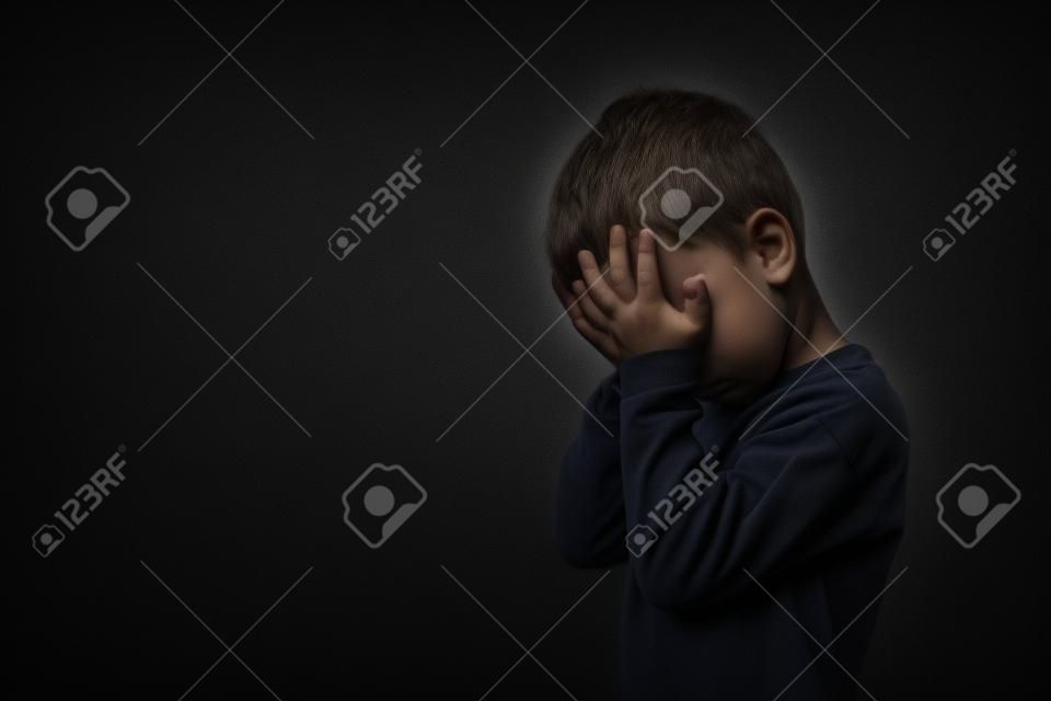 Kind, dessen Depression mit geschlossenen Händen auf schwarzem Hintergrund ist