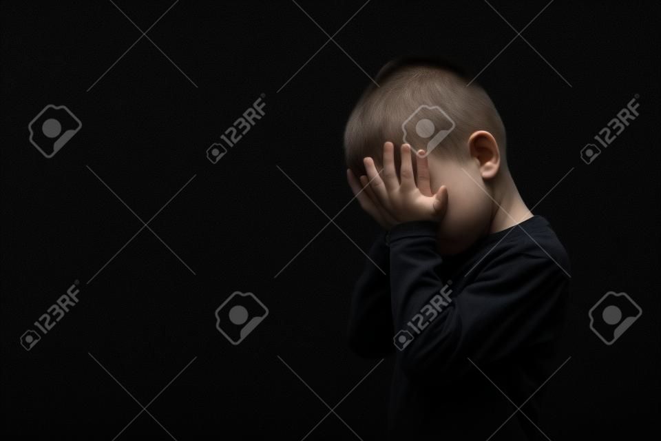 Criança cuja depressão está em um fundo preto com as mãos fechadas