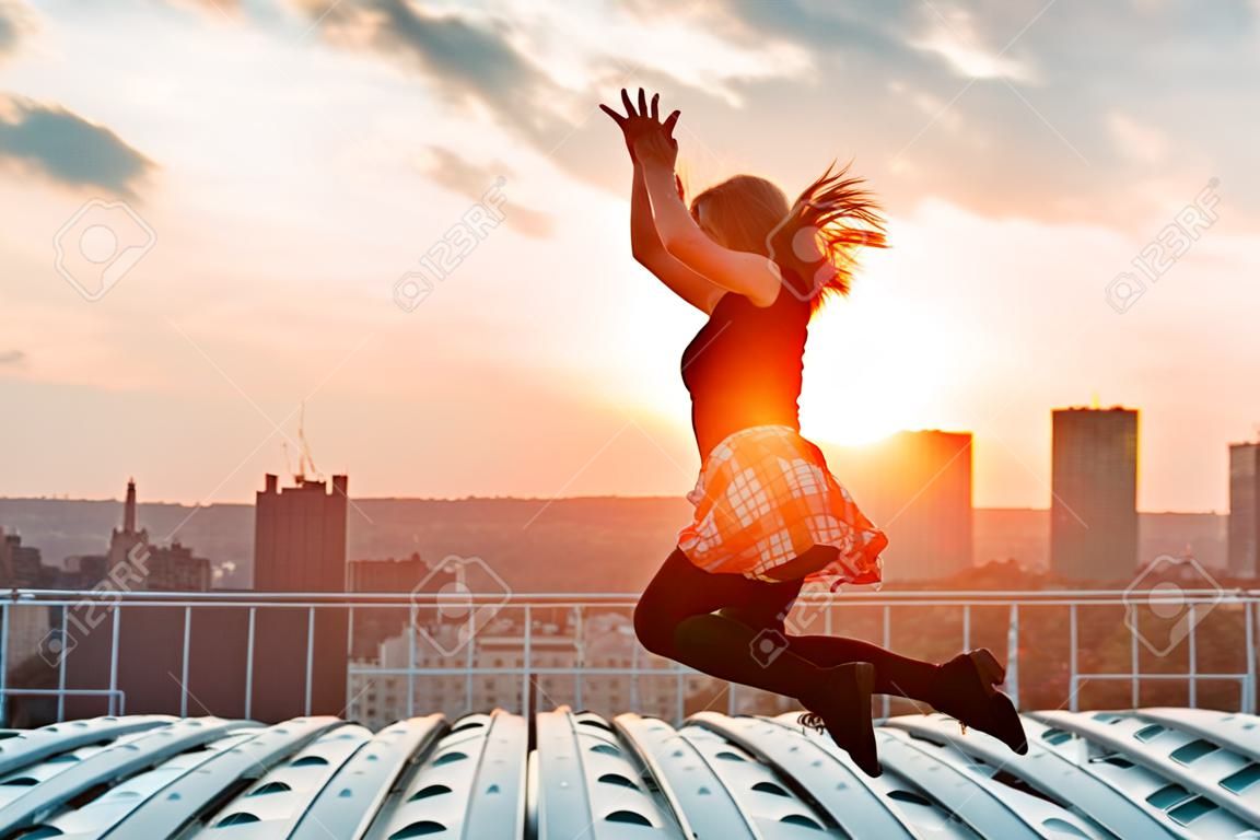 Silhueta de mulher alegre feliz pulando e se divertindo na cidade contra o pôr do sol. Conceito de liberdade e férias de lazer.