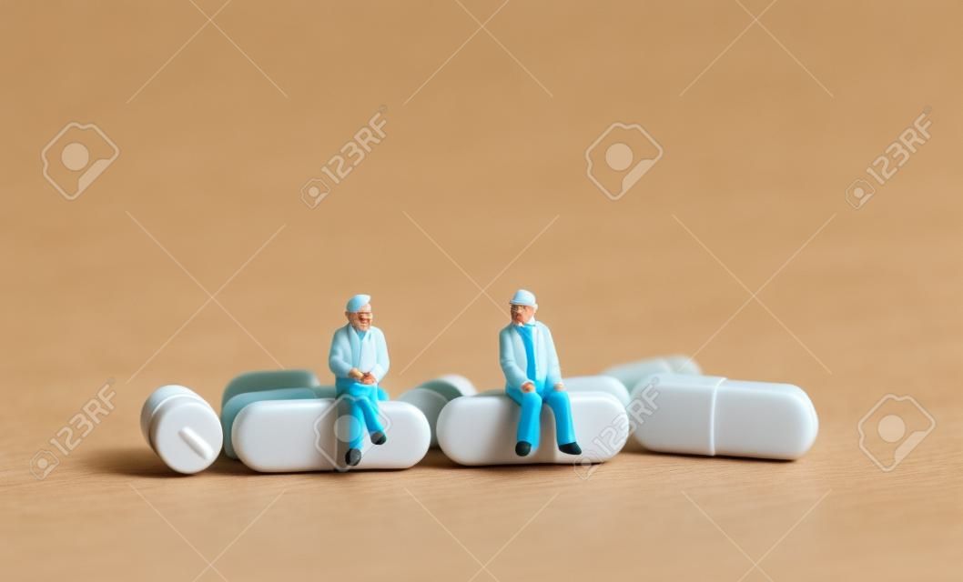 Pessoas em miniatura sentadas em pílulas. O conceito de pessoas idosas e cuidados de saúde.