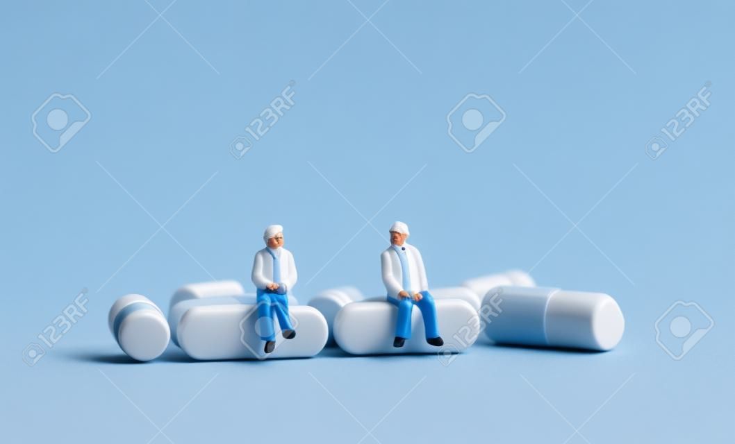 Miniature people sitting on pills. The concept of old people and health care.