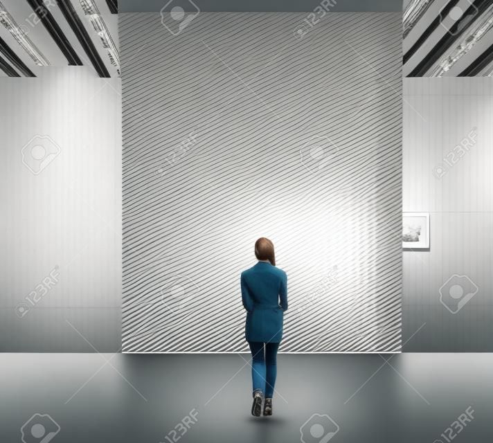 Giovane donna a piedi attraverso il corridoio di mostra ed esamina la galleria