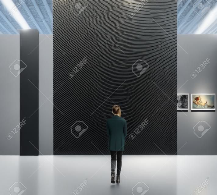 Young woman walking through on the exhibition hall and examines the gallery