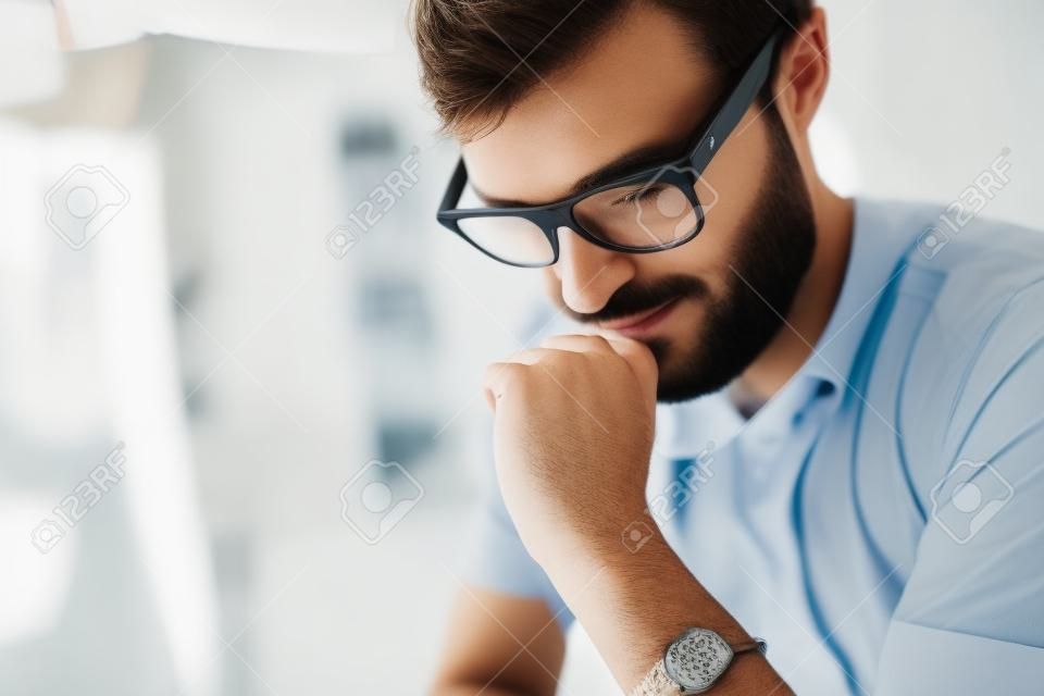 Closeup of portrait of attractive designer wearing eye glasses and working at the modern lightful office loft.Horizontal. Blurred background.