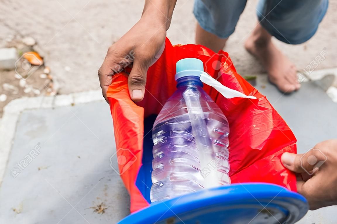 Male hand throwing empty plastic water bottle into recycling bin
