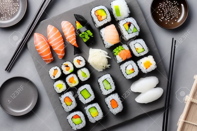 Conjunto de sushi japonês. Sashimi, rolos de maki e chá verde. Na placa de ardósia sobre fundo de pedra escura