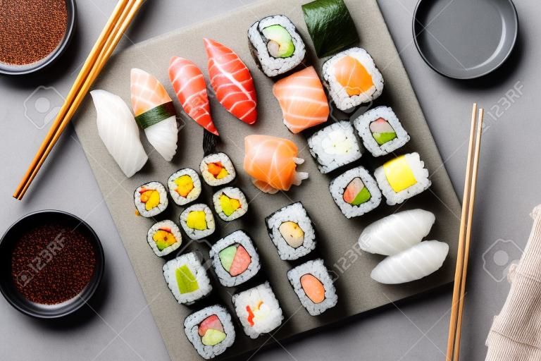 Japanisches Sushi-Set. Sashimi, Maki-Rollen und grüner Tee. Auf Schiefertafel über dunklem Steinhintergrund