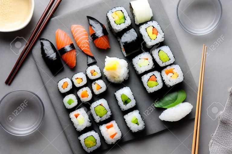 Conjunto de sushi japonês. Sashimi, rolos de maki e chá verde. Na placa de ardósia sobre fundo de pedra escura