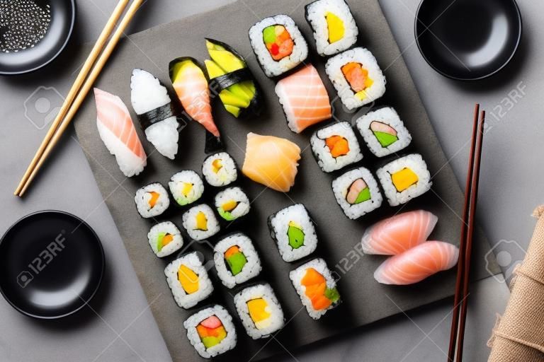 Japanisches Sushi-Set. Sashimi, Maki-Rollen und grüner Tee. Auf Schiefertafel über dunklem Steinhintergrund