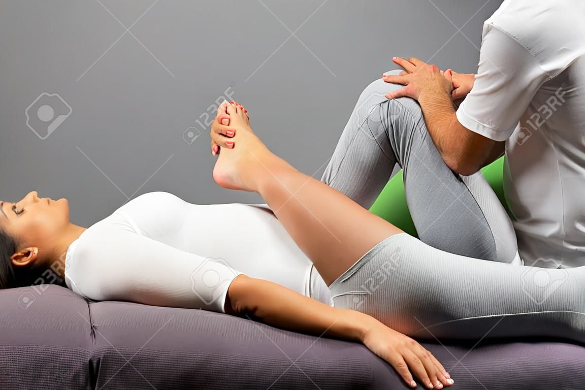 Feche acima do fisioterapeuta masculino que faz o tratamento manipulativo da perna na jovem mulher.