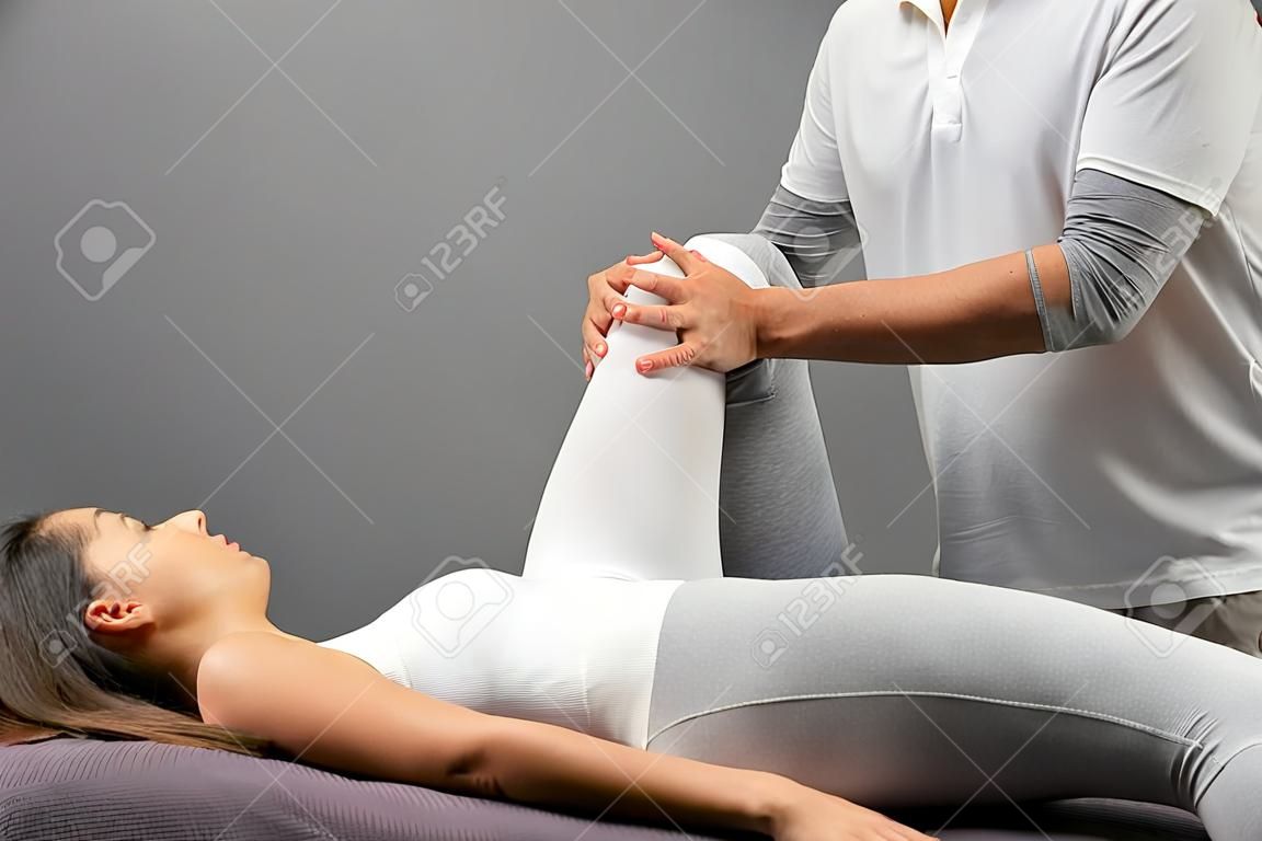 Feche acima do fisioterapeuta masculino que faz o tratamento manipulativo da perna na jovem mulher.