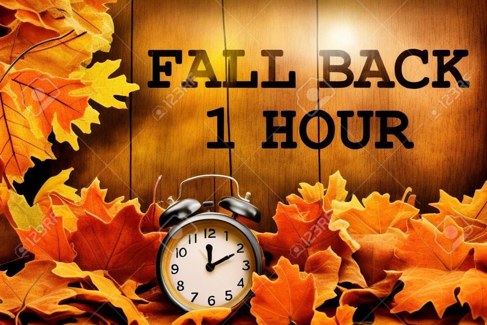 Changement d'heure d'automne, feuilles d'automne et réveil avec bois grunge avec texte Fall Back 1 Hour