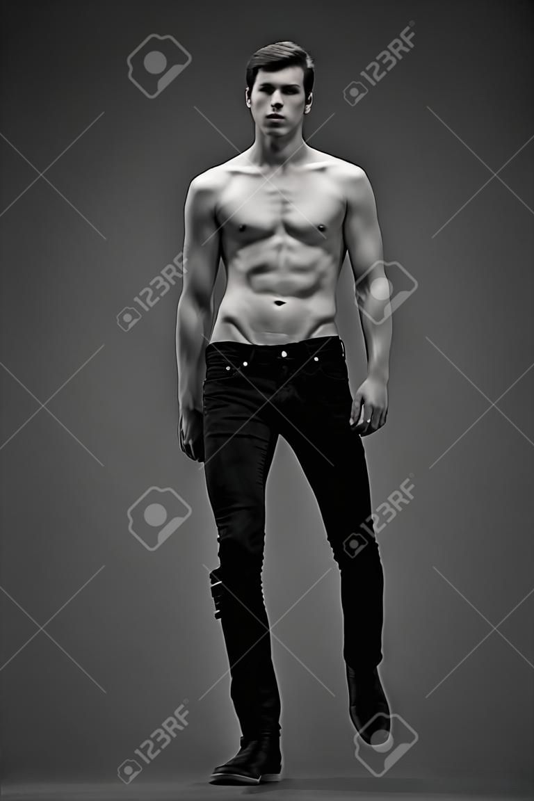 モデルをテストします。灰色の背景にポーズを完璧なボディと黒のジーンズでハンサムな男