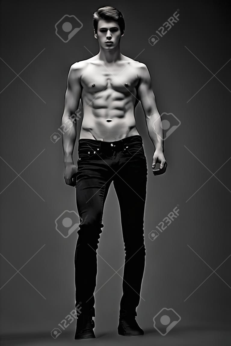 モデルをテストします。灰色の背景にポーズを完璧なボディと黒のジーンズでハンサムな男