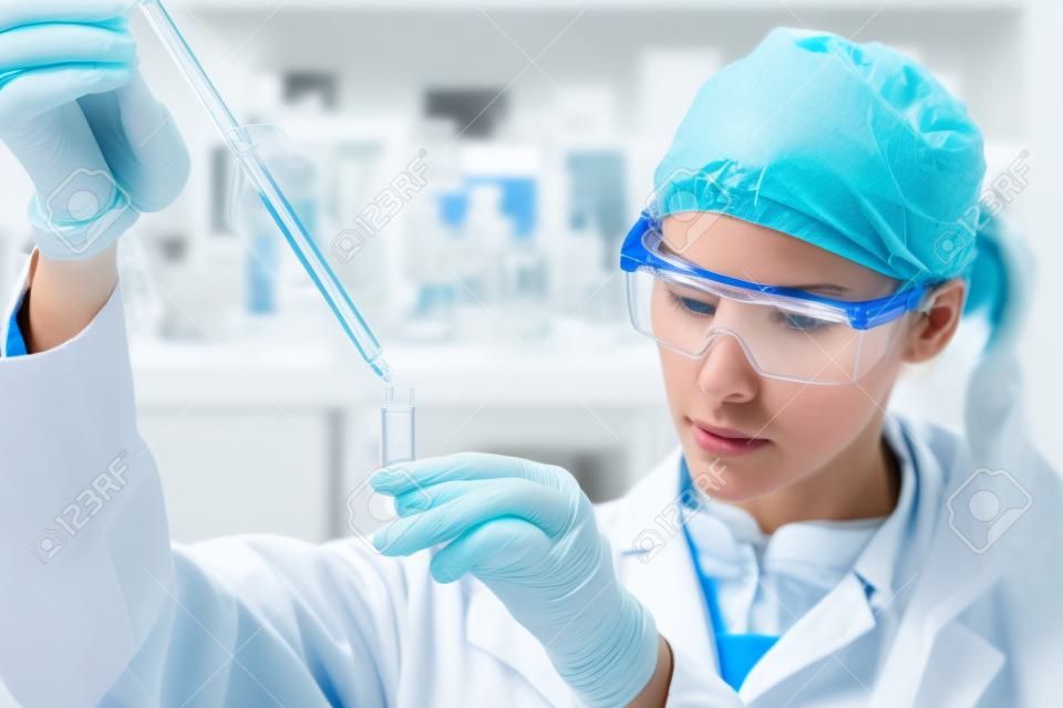 Life scientists researching in laboratory. Focused female life science professional pipetting solution into the glass cuvette. Lens focus on researcher's eyes. Healthcare and biotechnology concept.