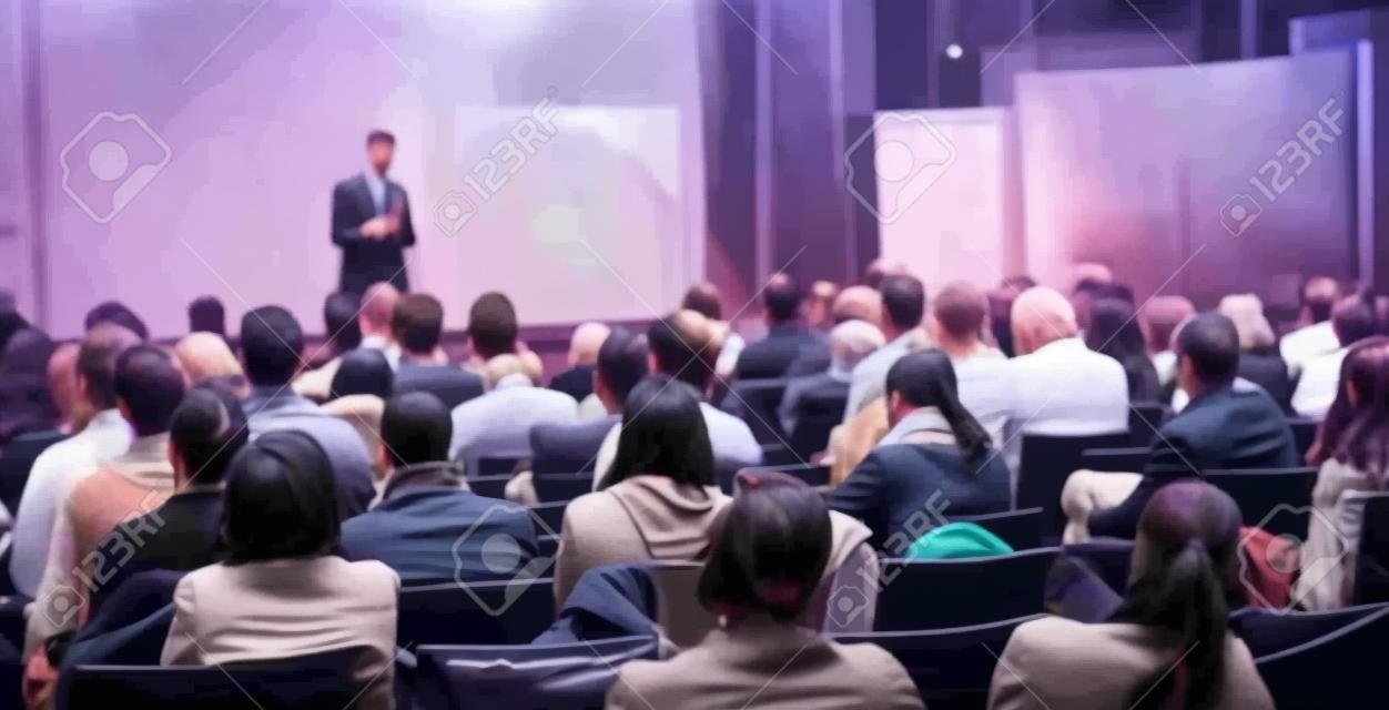 Speaker geeft een lezing in de conferentiezaal op business event. Achteraanzicht van onherkenbare mensen in het publiek in de conferentiezaal. Business en ondernemerschap concept.