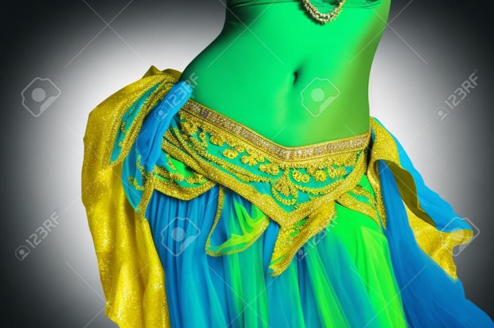 Close up shot of a belly dancer wearing a blue, gold and green costume shaking her hips  
