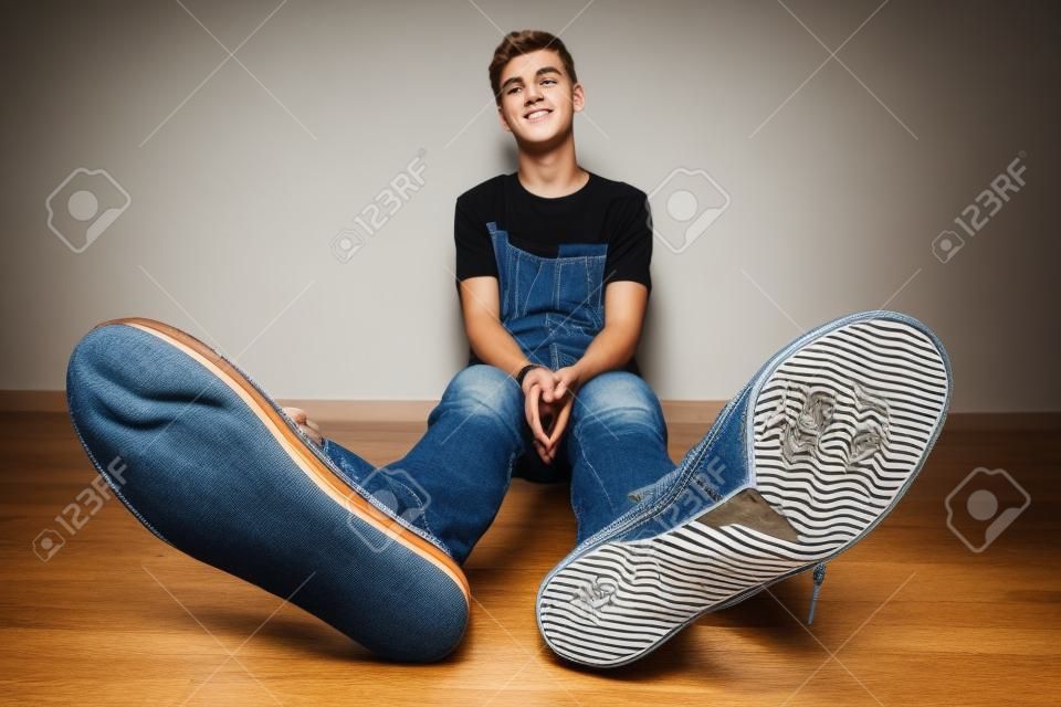 Adolescente si siede su un pavimento in camera in jeans e scarpe