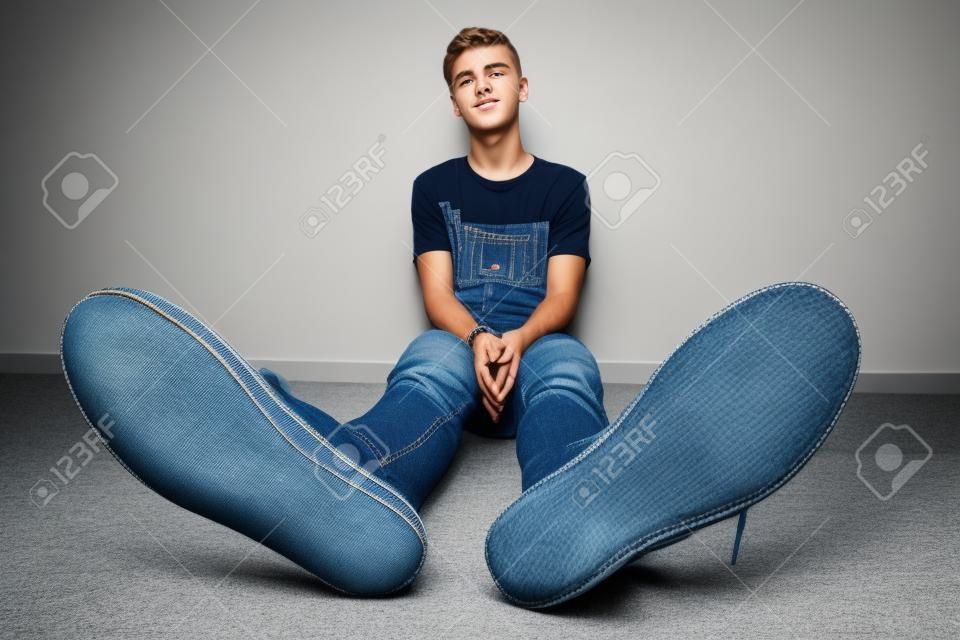 Adolescente si siede su un pavimento in camera in jeans e scarpe