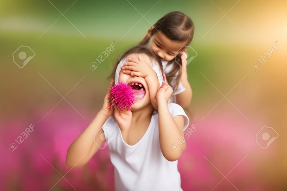 Fröhliches und verspieltes kleines Mädchen, das die Augen der Mutter von Hand bedeckt und eine Blumenüberraschung vorbereitet