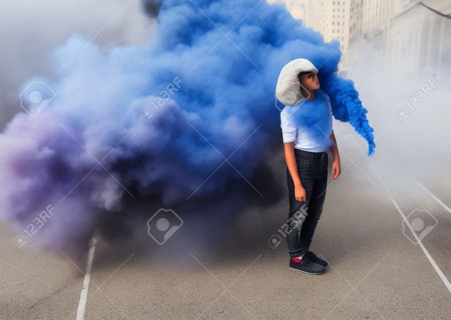 Adolescente con estilo de pie cerca de la bomba de humo en la ciudad