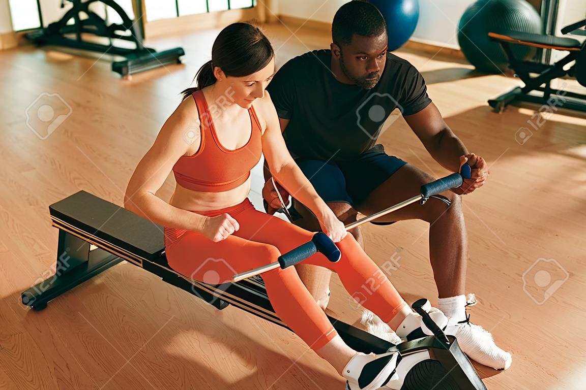Trainer helping sportswoman with exercise on rowing machine