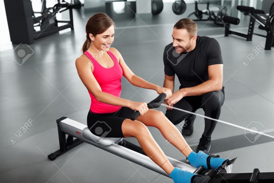Trainer helping sportswoman with exercise on rowing machine