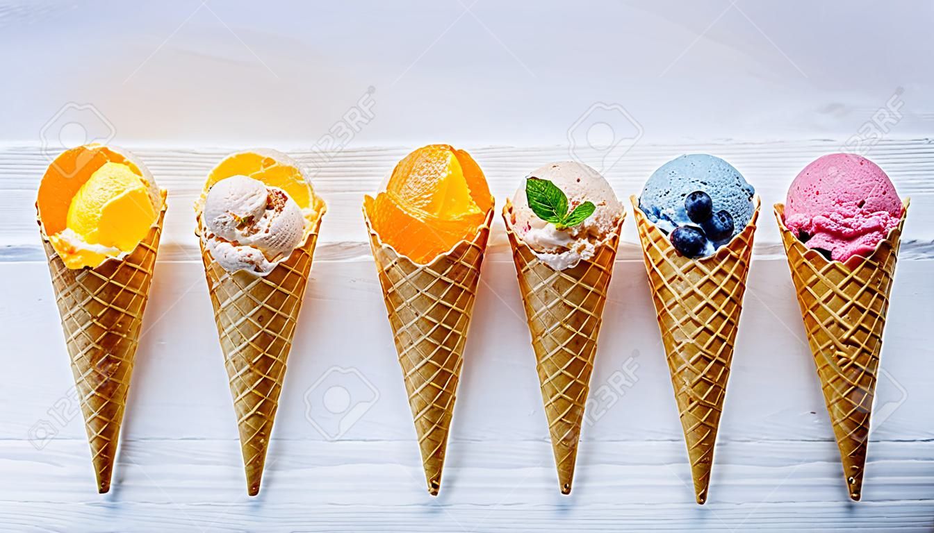 Diverses saveurs de crème glacée dans des cônes sur bois blanc