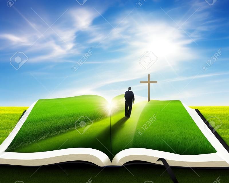 Otwarta Biblia trawą i mężczyznę idącego w kierunku krzyża