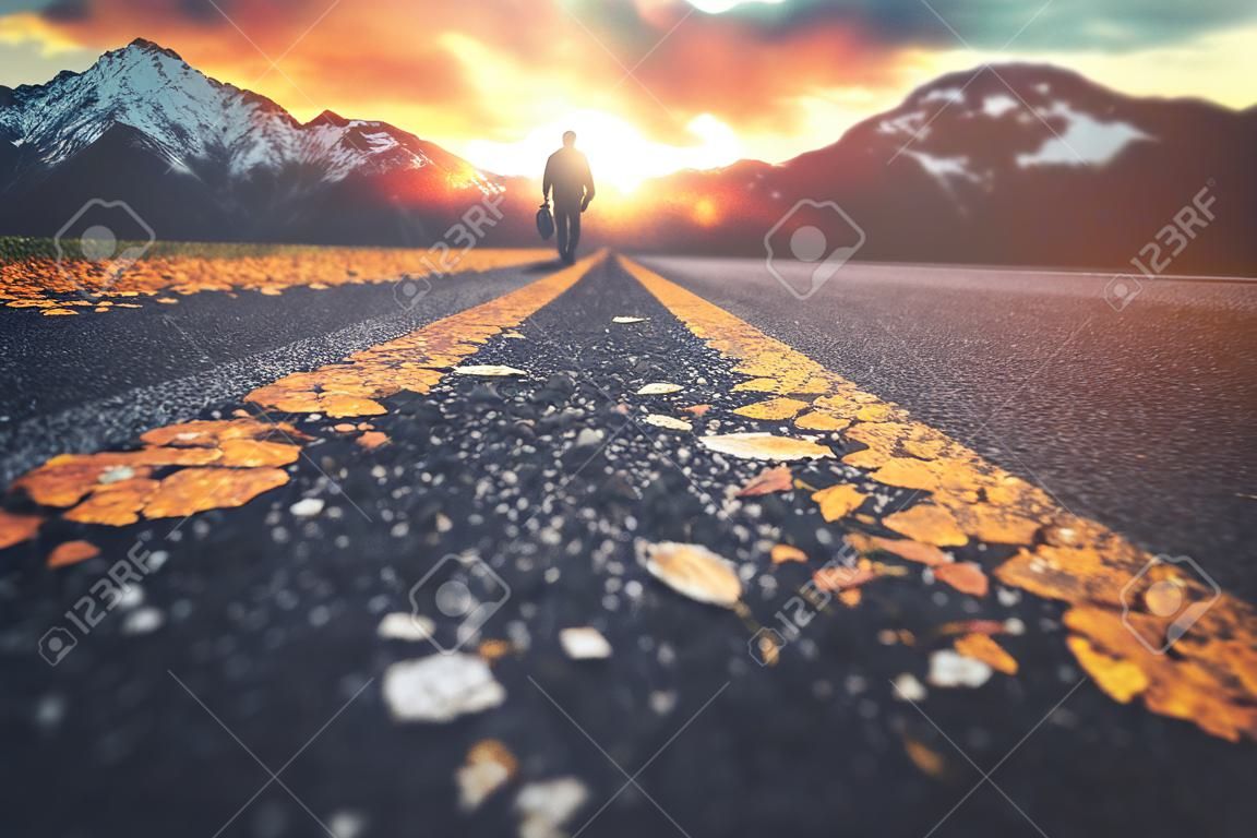 Un uomo che cammina lungo una strada verso un tramonto di montagna