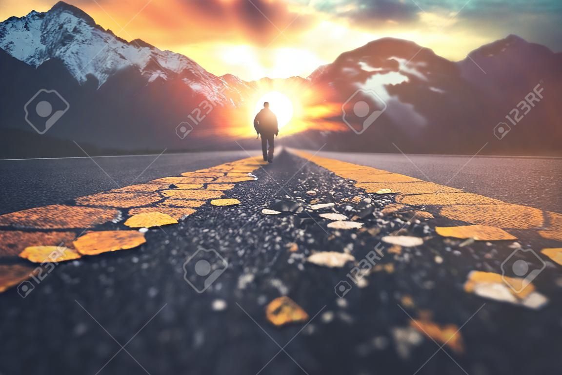 Un homme marchant sur une route vers un coucher de soleil sur la montagne