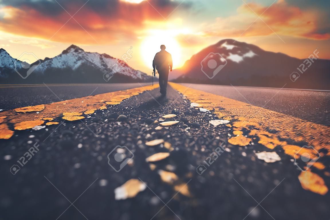 Un homme marchant sur une route vers un coucher de soleil sur la montagne