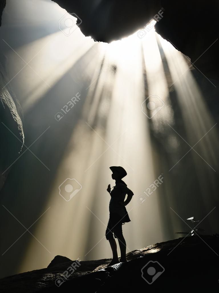 Silhouette of a woman in the cave with sun rays.