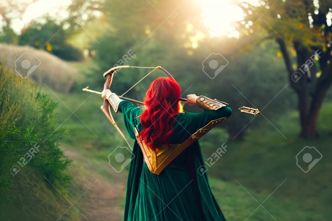 gorgeous huntress pushing her last light to the sun, waiting for salvation during terrible danger, red-haired girl fights bravely for life, emerald velvet cloak, photo without a face from the back