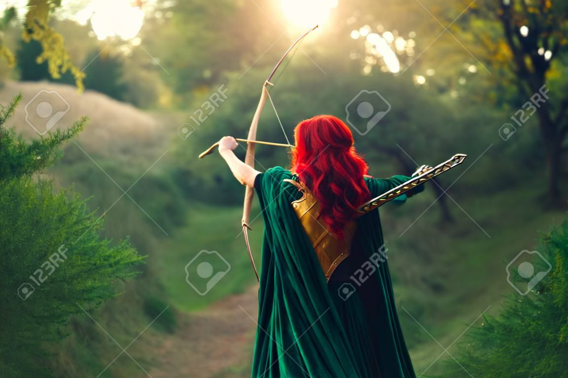 gorgeous huntress pushing her last light to the sun, waiting for salvation during terrible danger, red-haired girl fights bravely for life, emerald velvet cloak, photo without a face from the back