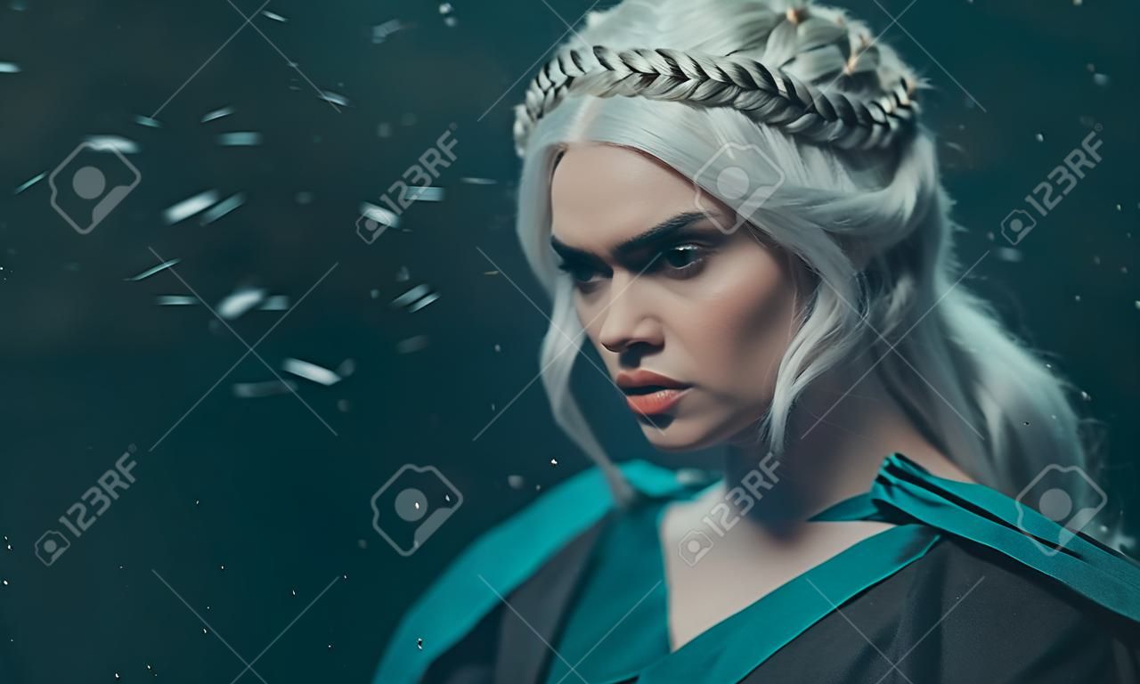 Porträt eines blonden Mädchens hautnah. Hintergrund dunkel mit fliegendem Schnee, Asche. Weißes Haar mit kreativem Flechten. Gefühle von Wut und Wahnsinn. Die Gothic-Königin in einer tiefen Winternacht. Kunstfoto