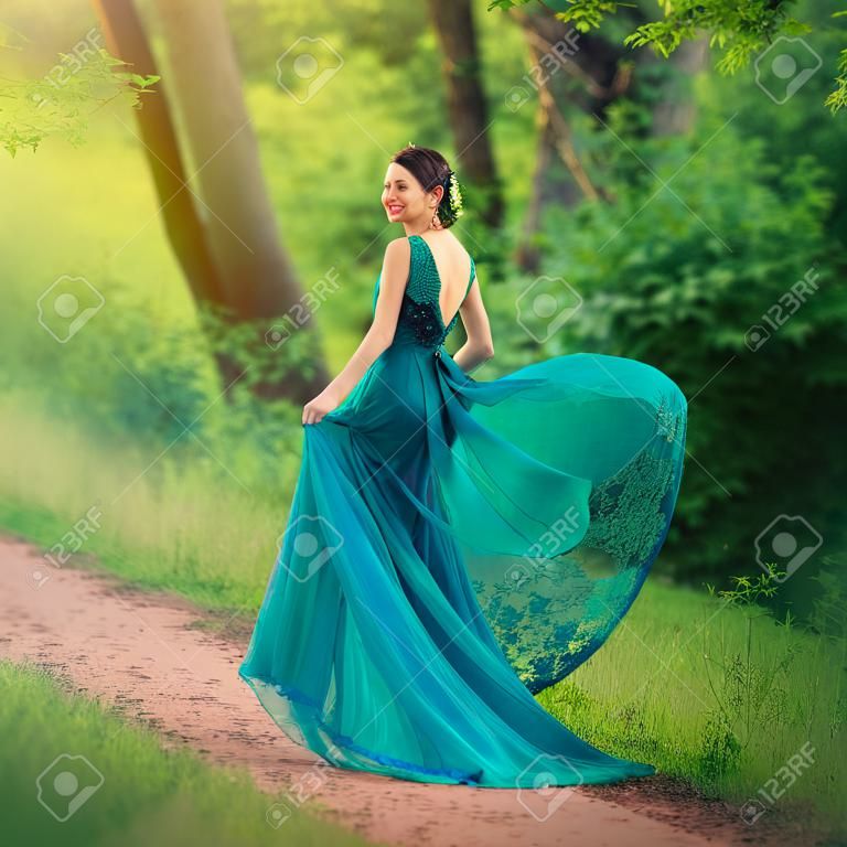 The girl in the evening, luxurious, Voter color dress, with an open back, with a flying train, goes along the path. The image of the party, a young charming graduate with good taste. Elegant lady.