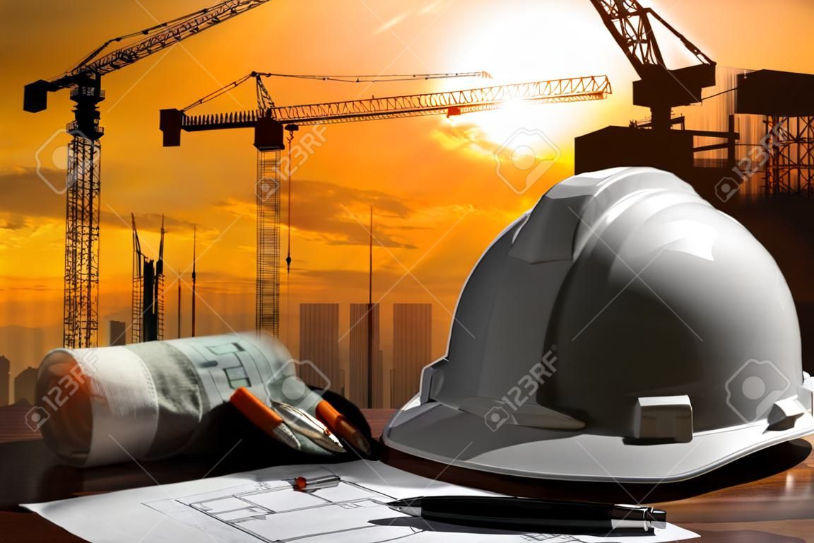 arquivo de capacete de segurança e arquiteto aplainado na mesa de madeira com cena do pôr do sol e construção de edifícios