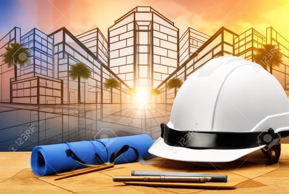 safety helmet and architect plan on wood table with sunset scene and building construction