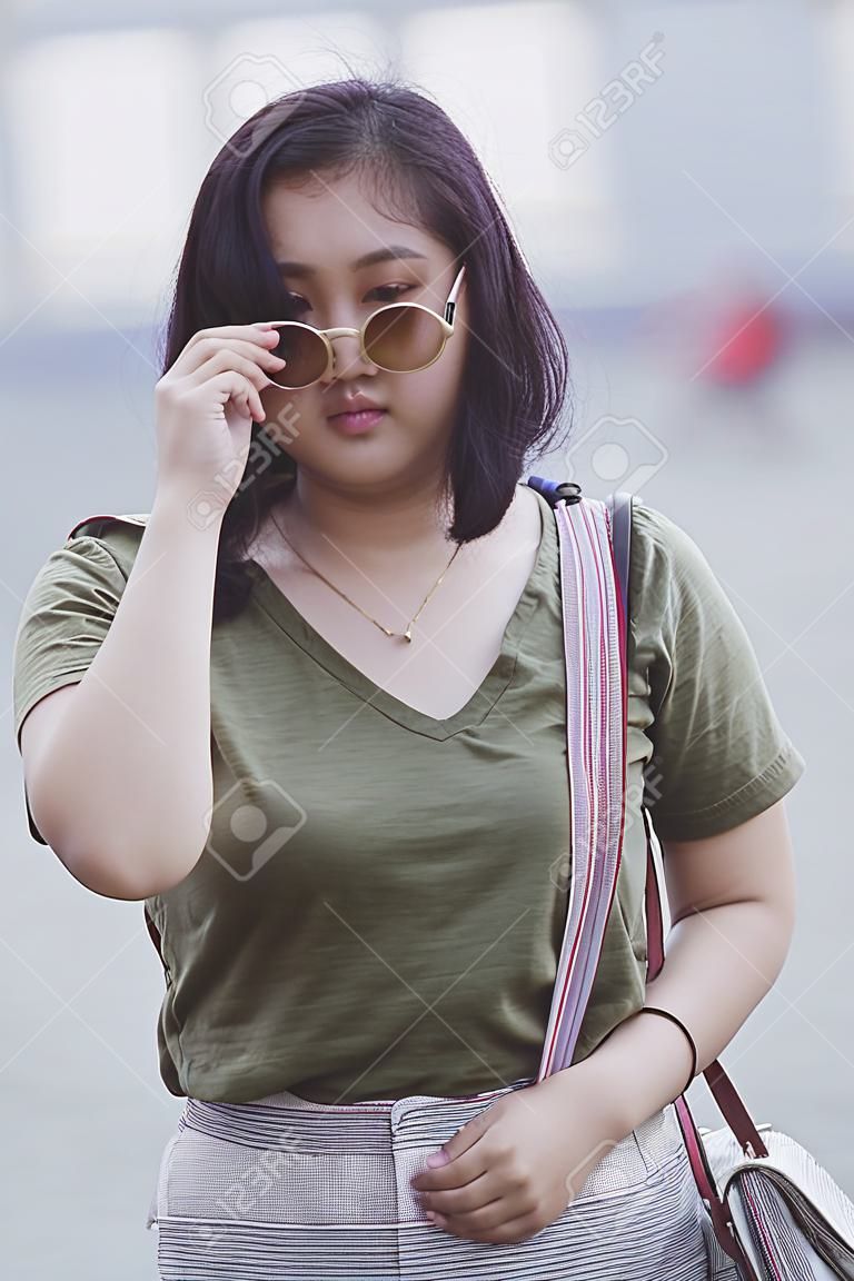 Adolescente asiático con gafas de sol de pie con confianza en sí mismo