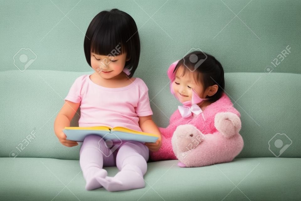 Asiático libro chino de lectura niña con osito de peluche en el sofá de la sala de estar.