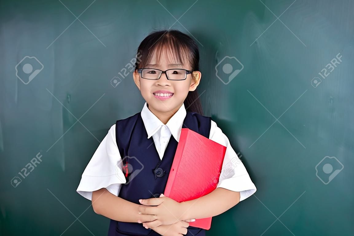 Asian Chinese little Girl in uniform standing against green blackboard in classroom