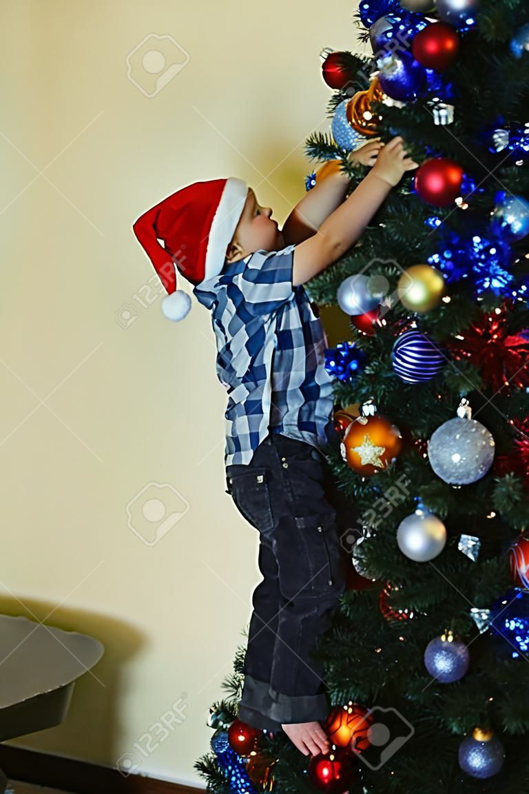 Little boy decorating the Christmas tree trying to reach as high as possible