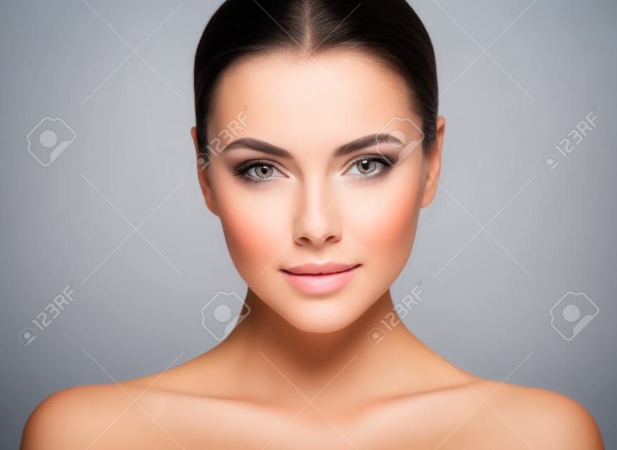Beauty Woman face Portrait. Beautiful Spa model Girl with Perfect Fresh Clean Skin. Brunette female looking at camera and smiling. Youth and Skin Care Concept. Gray background