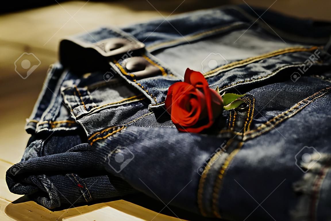 Blue jeans folded with red rose on wooden table and on wooden background.