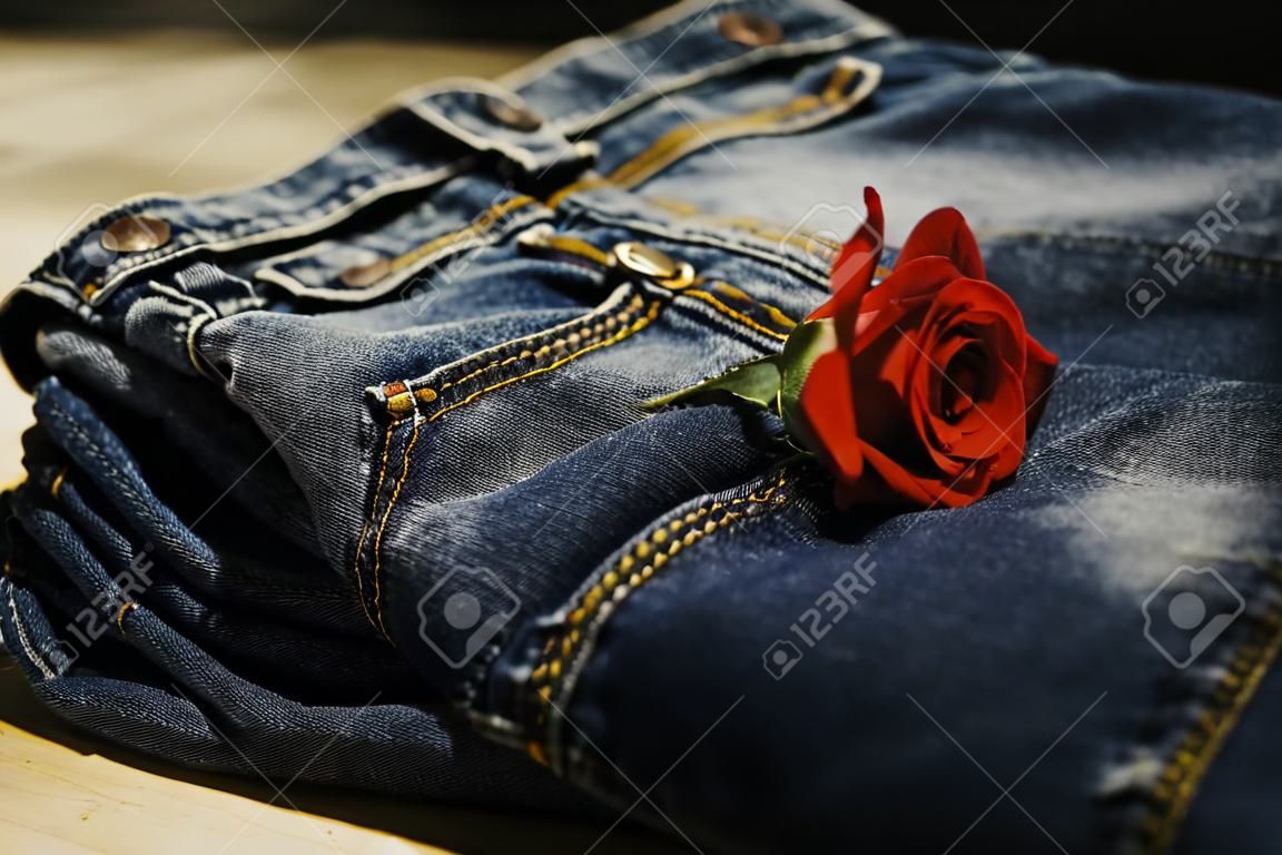 Blue Jeans falteten sich mit Rotrose auf Holztisch und auf hölzernem Hintergrund.