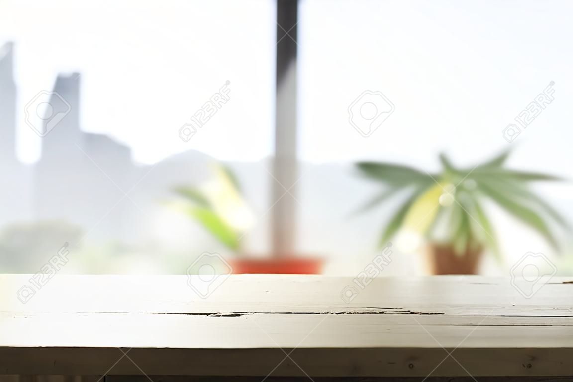 Holztischplatte auf verschwommenem Fensterglas und abstraktem Grün vom Garten mit Blick auf die Stadt am Morgen im Hintergrund. Zur Montage der Produktpräsentation